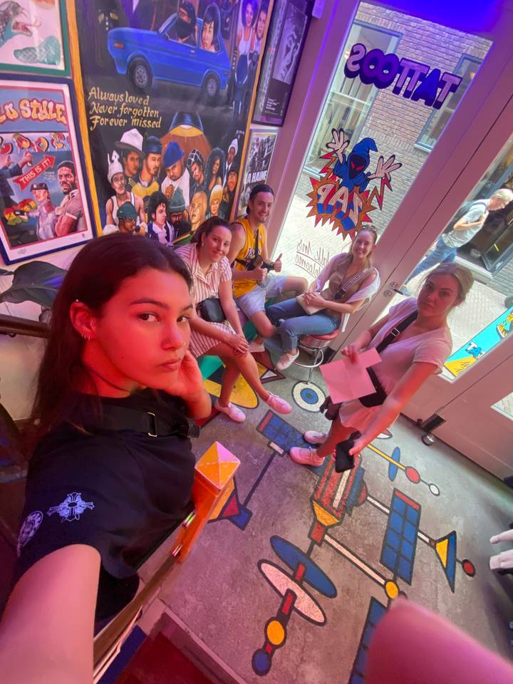 Group of people sitting on a colorful floor, with a sign reading 'TATTOO'.