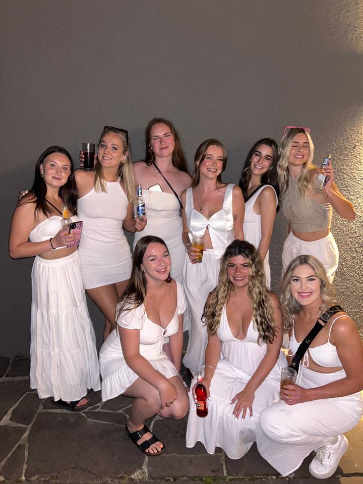 Group of women in white dresses posing against a wall.