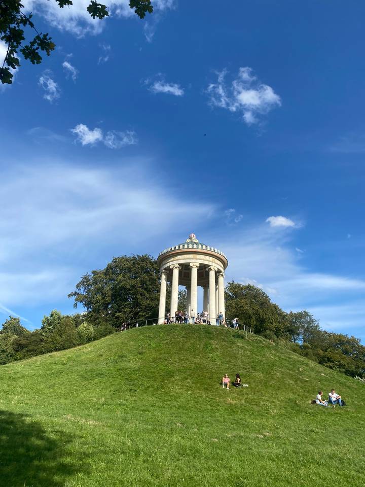 White columned rotunda on a grassy hill under a blue sky.