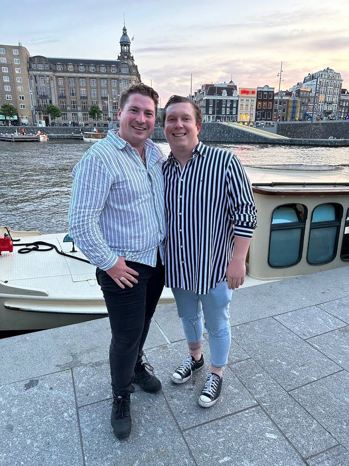 Two people posing by a waterway in a city with boats and bicycles.