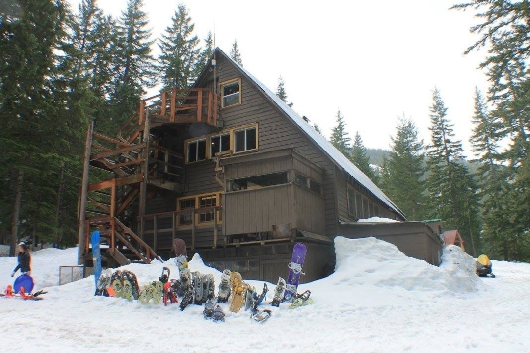 A wooden lodge surrounded by snow, with snowboards and snowshoes at the entrance.