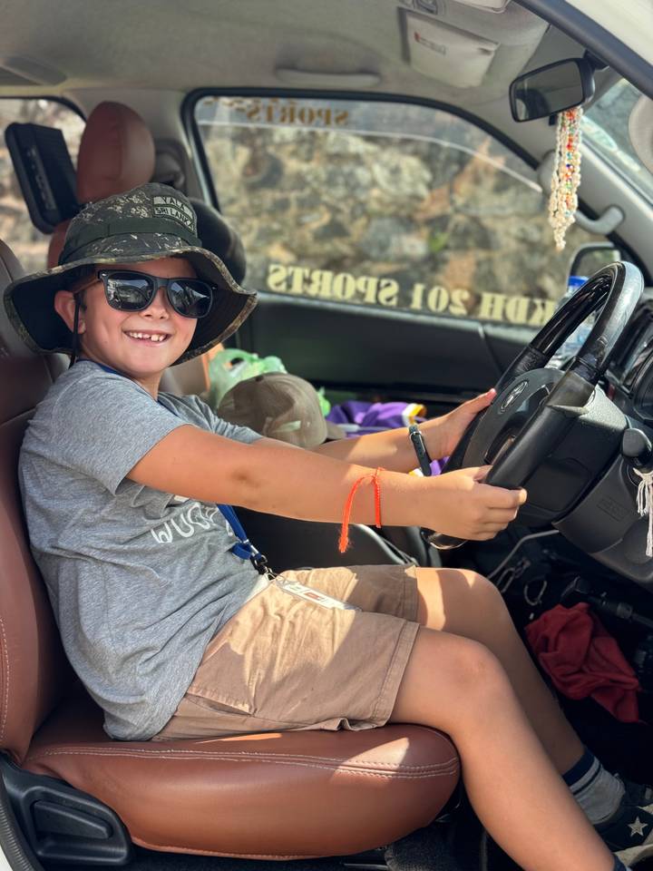 Kind poseert speels op de bestuurdersstoel van een voertuig.