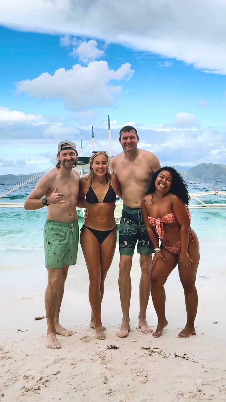 Vier mensen die genieten van het strand met een boot op de achtergrond.