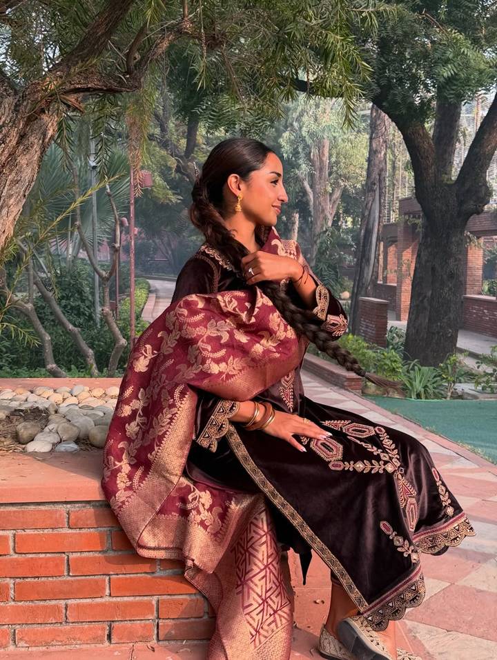 Une femme assise à l'extérieur avec une broderie détaillée sur ses vêtements.