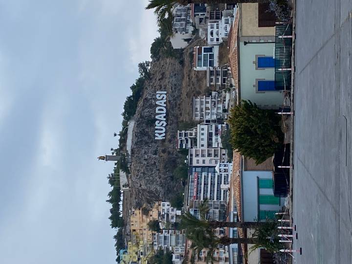 Vue de colline avec un grand panneau 'KUSADASI' et des bâtiments résidentiels en contrebas.