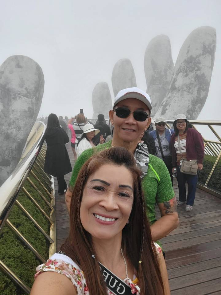 Toeristen op een mistige brug met grote stenen handen.