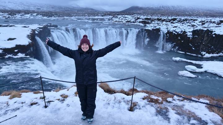 Persona sonriente con vestimenta de invierno posando frente a una cascada.