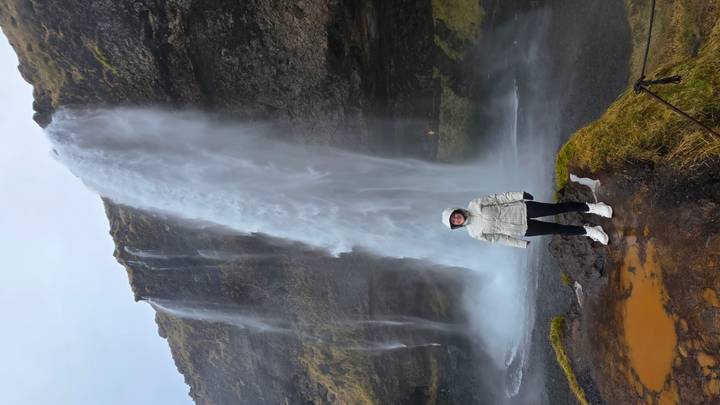 Persona posando frente a una cascada alta.