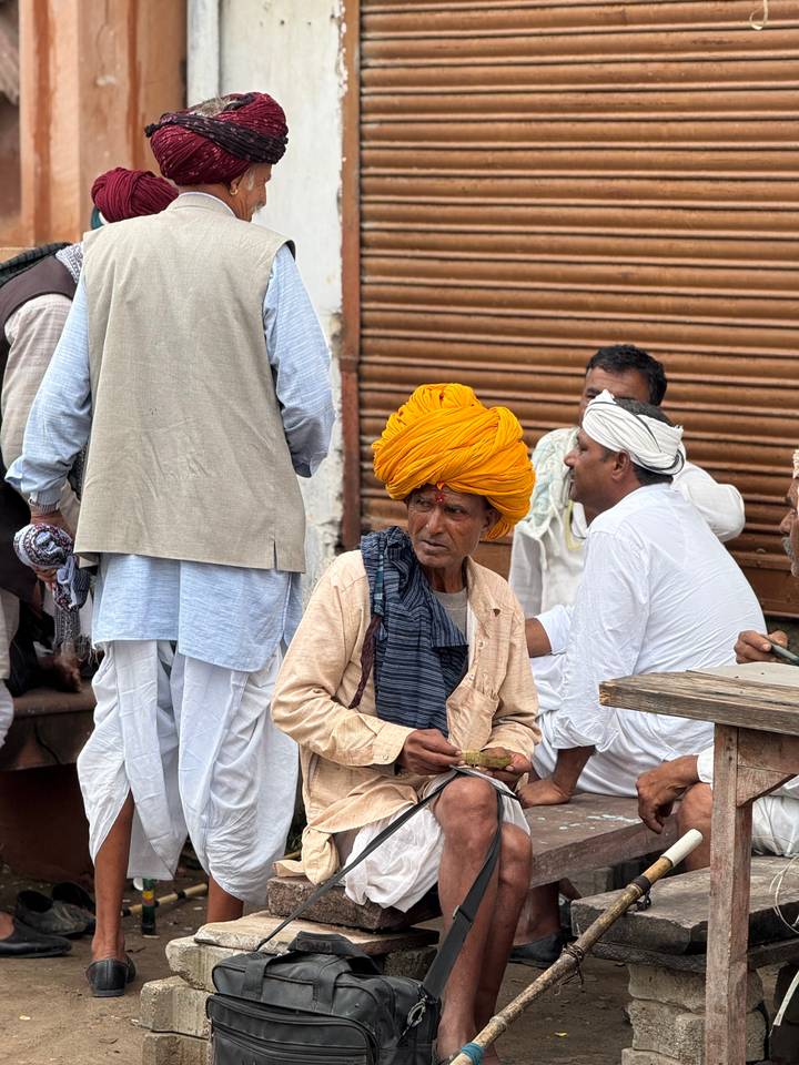 Hombre anciano con un turbante brillante sentado afuera de una tienda.