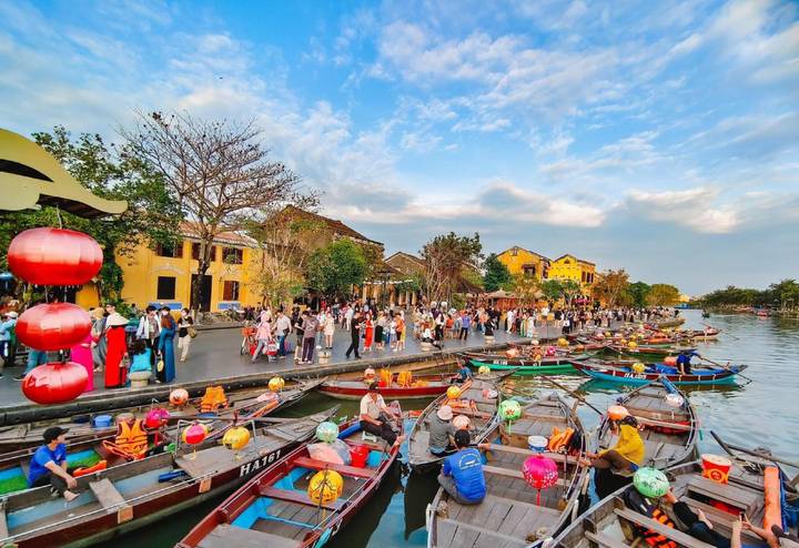 Front de mer animé à Hoi An avec des bateaux colorés et des foules.