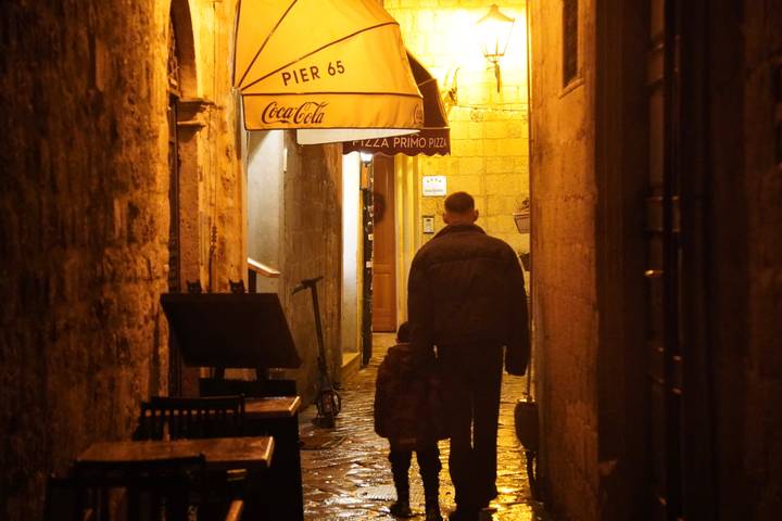 Deux personnes marchant dans une ruelle étroite faiblement éclairée avec des parapluies et des enseignes de café.