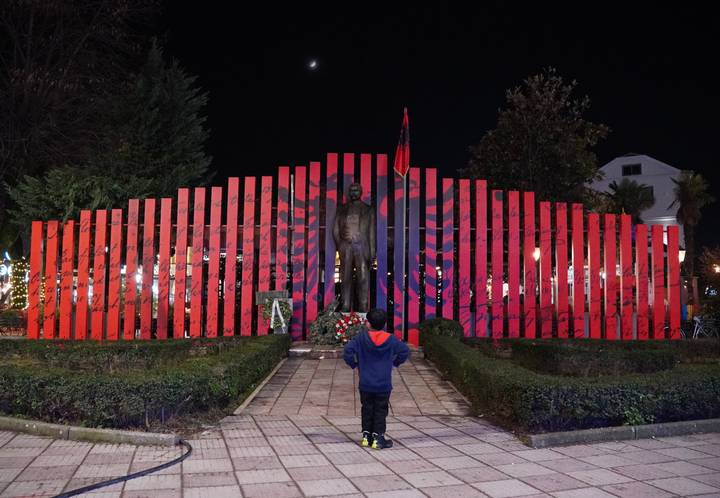 Enfant debout devant une statue avec un arrière-plan de drapeaux.