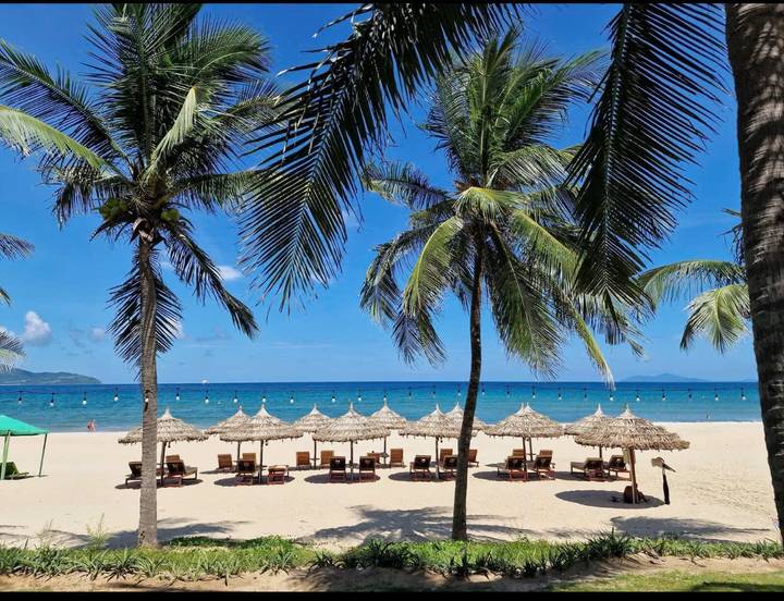 Schöner Strand mit Strohsonnenschirmen und klarem blauem Meer.