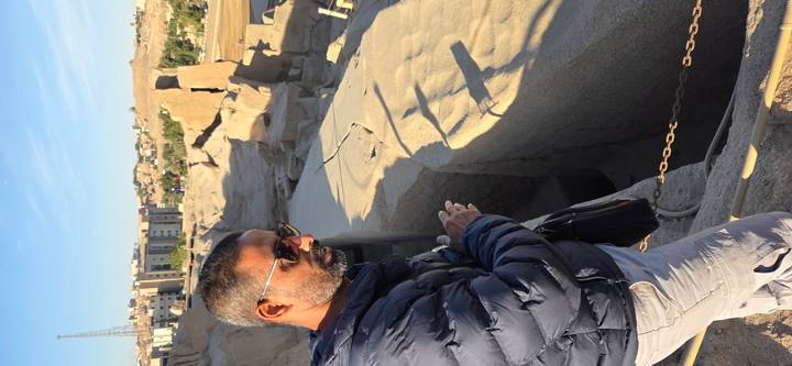 Un hombre de pie cerca de ruinas antiguas con paisaje desértico de fondo.