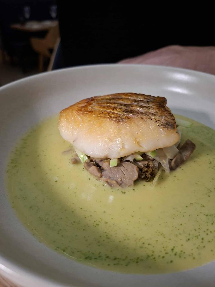 Un plato servido con pescado sobre una cama de verduras.
