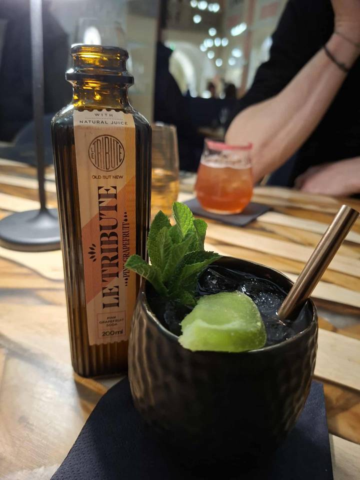 Una bebida con una guarnición de menta y una botella de bebida.