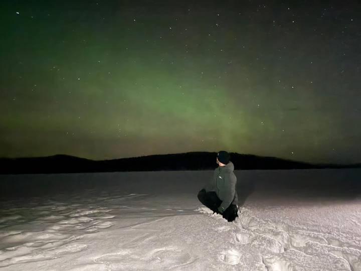 Persona sentada en la nieve observando la aurora boreal.