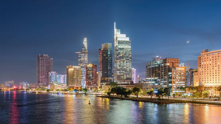 Vue nocturne d'un horizon urbain avec des bâtiments illuminés se reflétant sur une rivière.