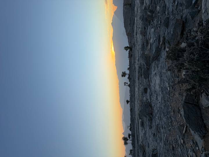 Vista del atardecer sobre un paisaje rocoso árido con árboles en silueta.