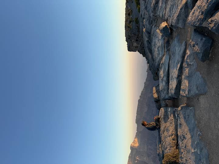 Persona sentada en una colina rocosa con amplia vista de montañas durante el atardecer.