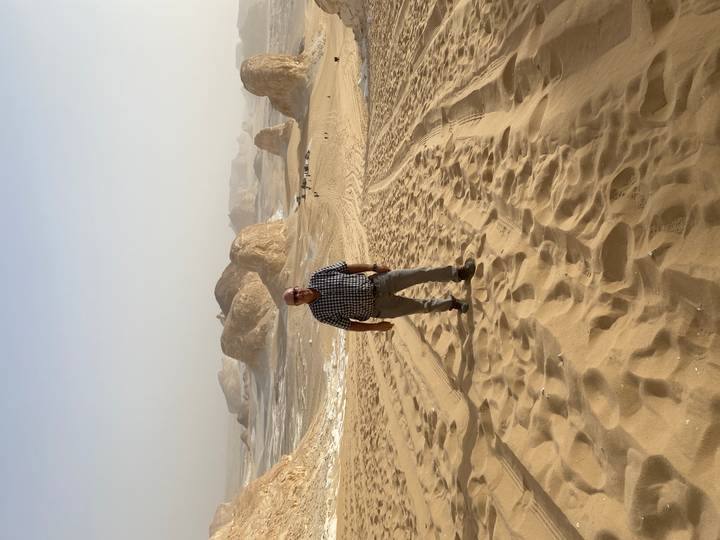 Persona de pie en un paisaje desértico arenoso con formaciones rocosas.