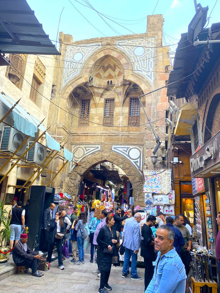Escena bulliciosa de mercado con arco de piedra ornamentado arriba.