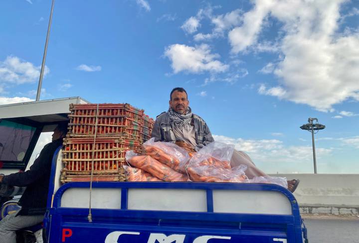 Hombre sentado en un camión cargado con bolsas de mercancías con un cielo despejado.