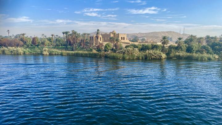 Paisaje exuberante junto a un gran río con edificio histórico.