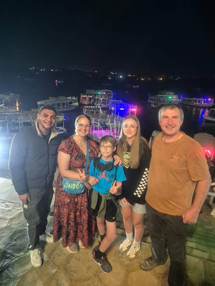Famille posant devant des bateaux illuminés la nuit.