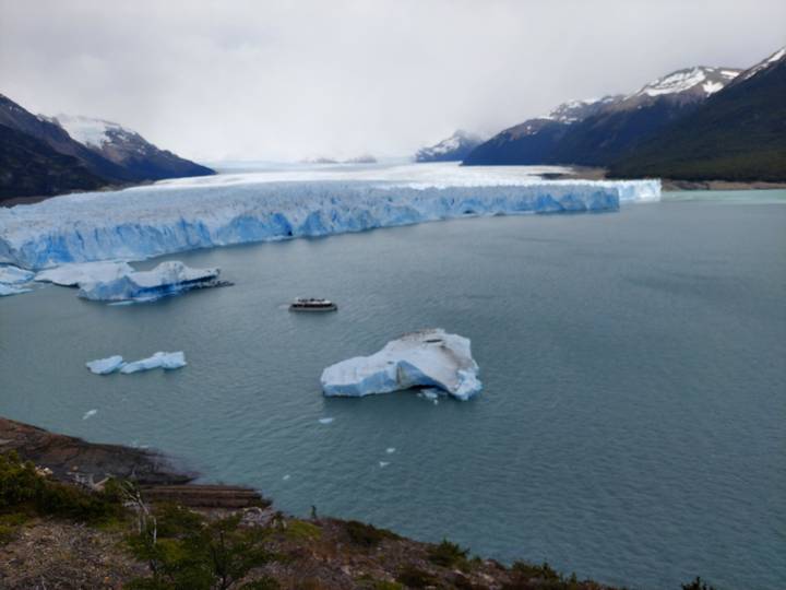 Icebergs dans un grand lac gelé avec des glaciers lointains sous un ciel nuageux.
