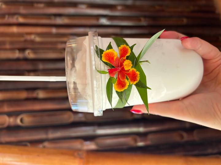 Boisson froide dans un gobelet en plastique avec une paille et une garniture florale.