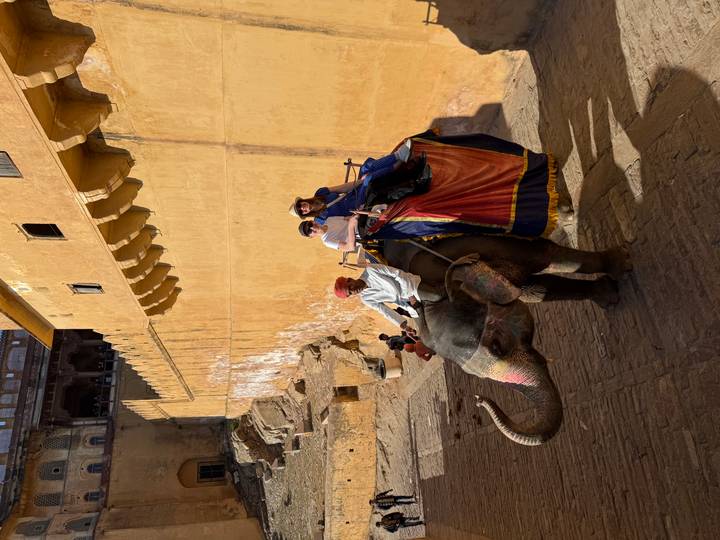 Pareja montando un elefante a lo largo de las murallas de un fuerte histórico.
