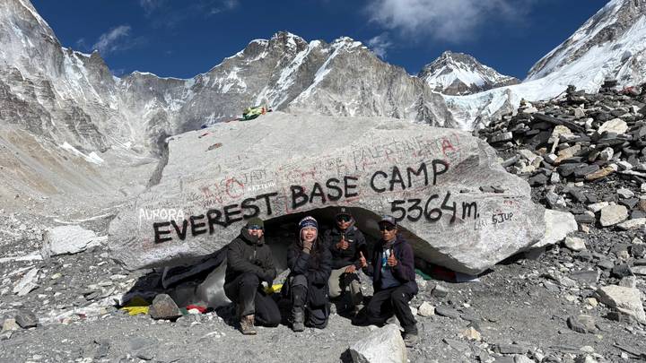 Grupo de personas posando frente a un letrero en un campamento base de montaña.
