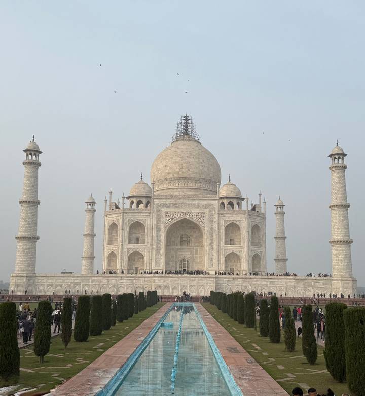 Taj Mahal bajo un cielo brumoso con visitantes.