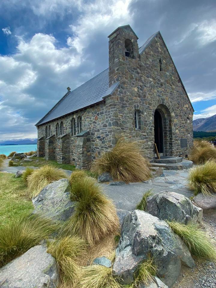 Église en pierre près d'un lac sous un ciel partiellement nuageux.