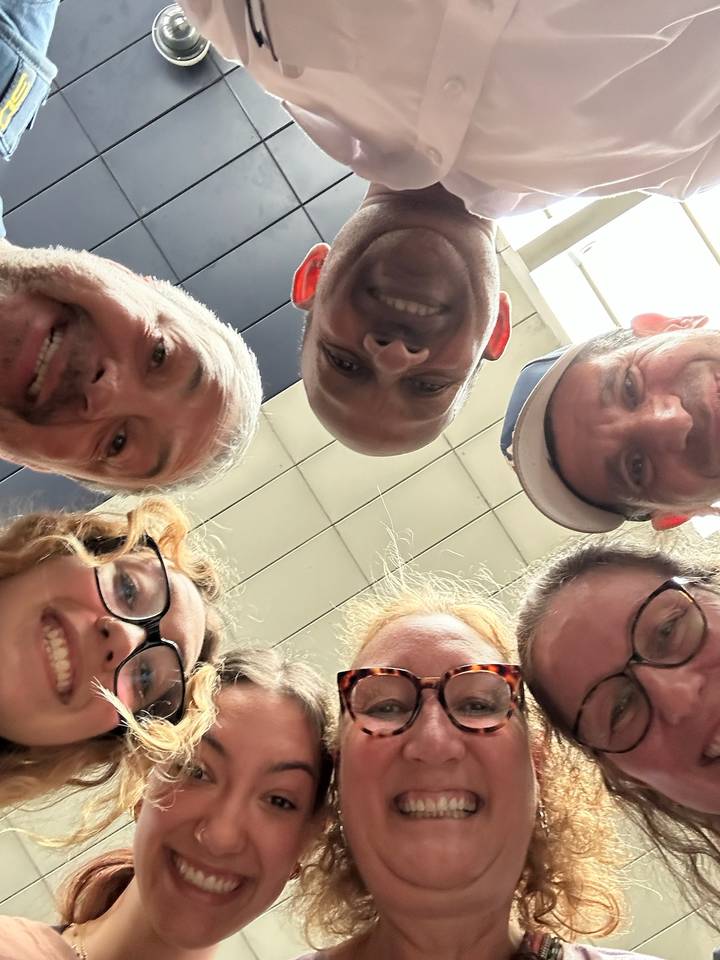 Selfie de groupe pris en contre-plongée montrant plusieurs personnes souriantes.