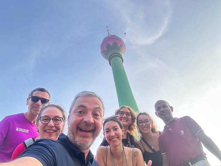 Groupe posant avec une haute tour en arrière-plan sous un ciel bleu.