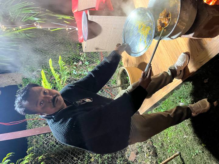 Hombre cocinando comida en una estufa al aire libre por la noche.