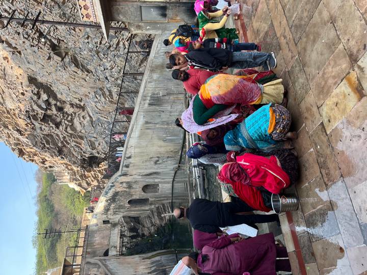 Grupo de personas con vestimenta colorida reunidas junto a un cuerpo de agua.