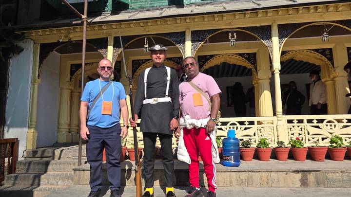 Trois personnes posent en tenue traditionnelle devant un bâtiment.