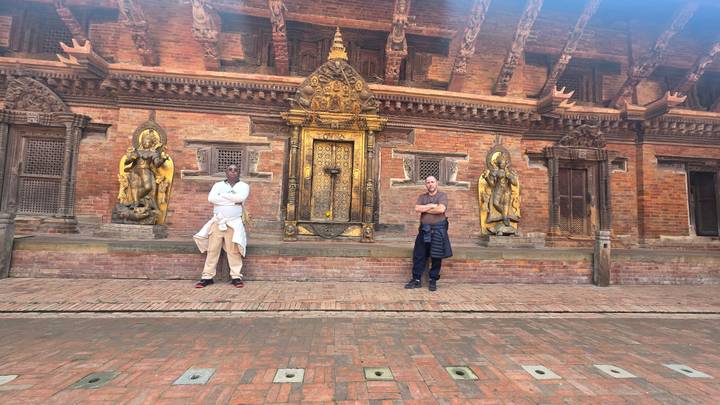 Deux personnes debout devant un bâtiment historique avec des boiseries ornementées.