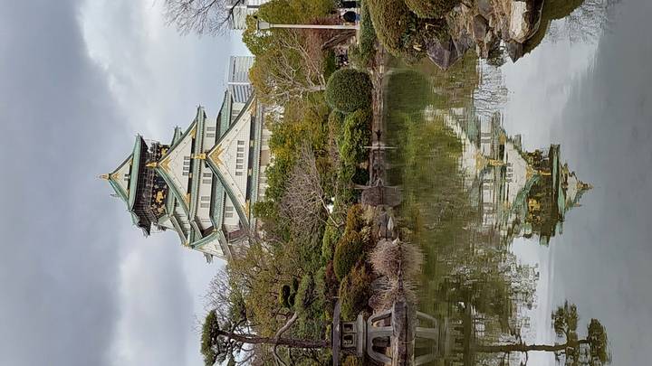 Osaka Castle reflected in a pond surrounded by greenery.