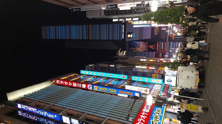 Rue animée à Shinjuku avec panneaux publicitaires et passants.