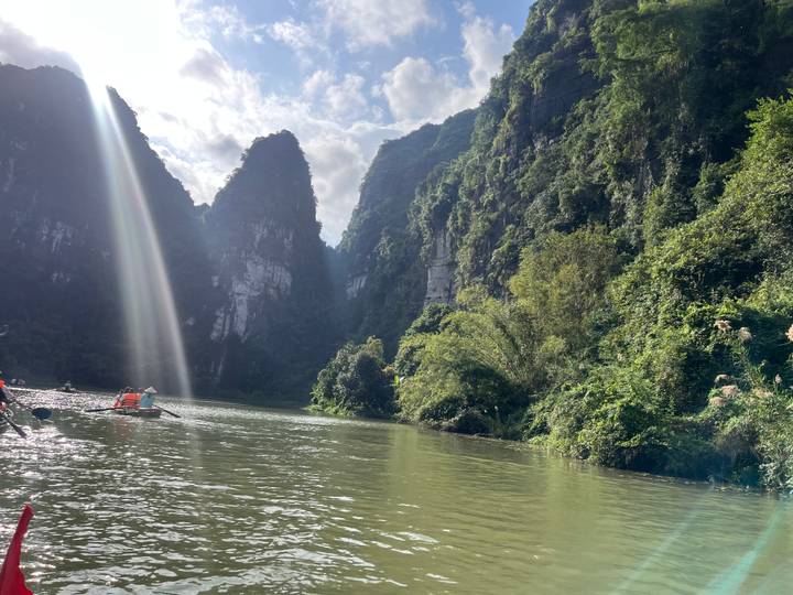 Rivière ensoleillée avec des falaises calcaires luxuriantes et un bateau en bois.