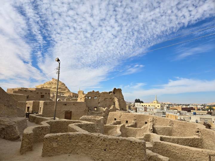 View of the Shali Fortress ruins in Siwa Oasis under a cloudy blue sky.