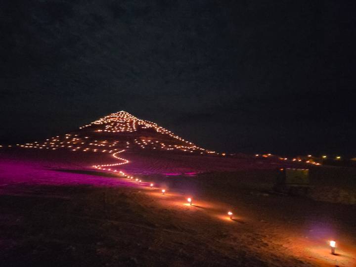 A hill covered in lights at night, with torches illuminating a path leading up.