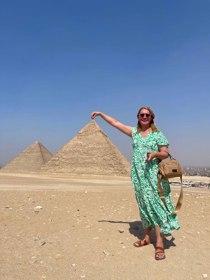 Femme posant comme si elle tenait la pointe d'une pyramide devant les Pyramides de Gizeh.