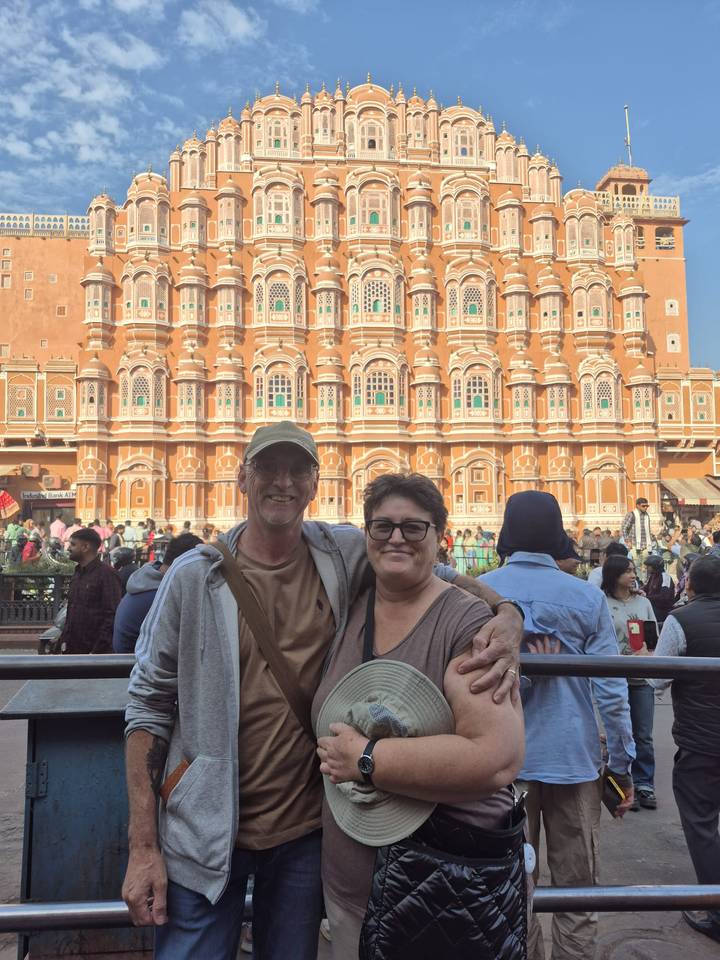 Pareja posando frente al icónico Hawa Mahal rosa, con una multitud bulliciosa.