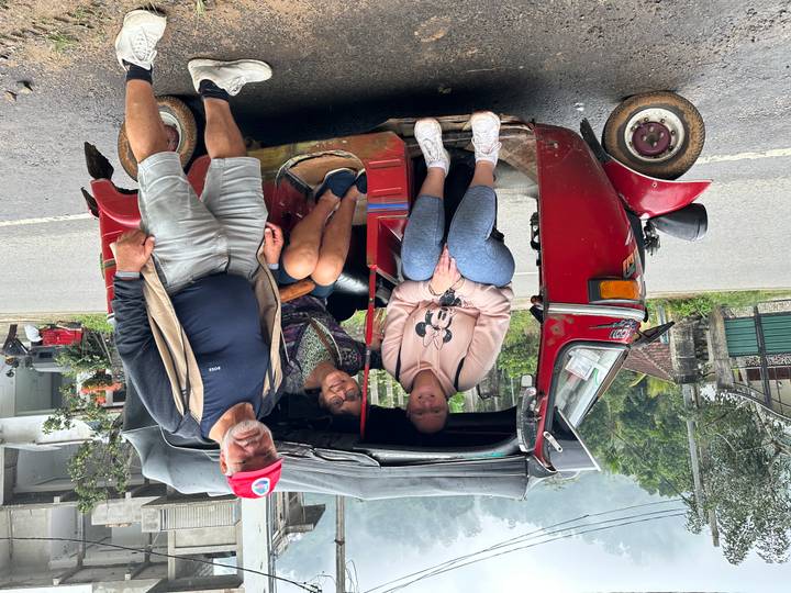 Trois personnes posant avec un tuk-tuk rouge dans une rue.