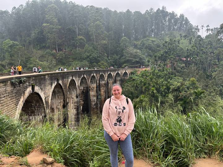 Une personne posant sur un pont pittoresque entouré d'une végétation luxuriante.